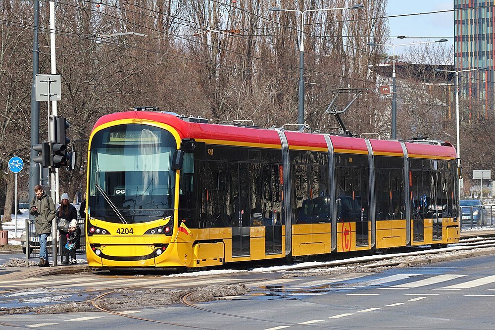 Modern gul och röd spårvagn 4204 på stadsgata med passagerare som väntar vid spårvagnshållplats på vintern