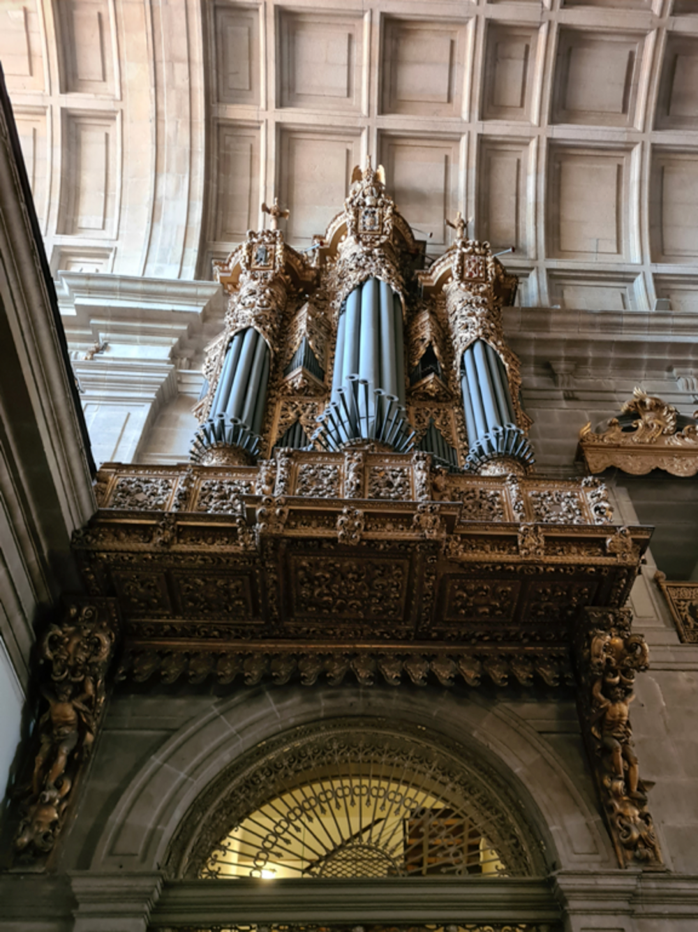 Ornate antik piporgel med intrikata guldsniderier inuti en historisk katedral med stenbågar
