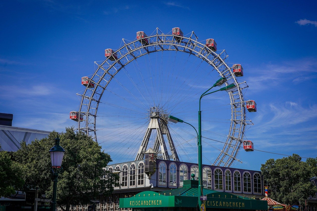 Stort pariserhjul med röda kabiner på en nöjespark under en klarblå himmel under dagtid