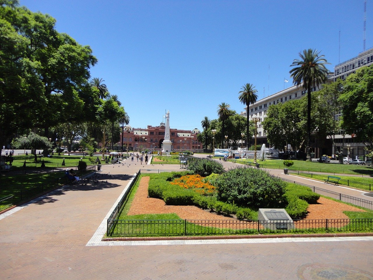 Solig dagvy av Plaza de Mayo med gröna trädgårdar, palmer och Casa Rosada presidentpalats i Buenos Aires