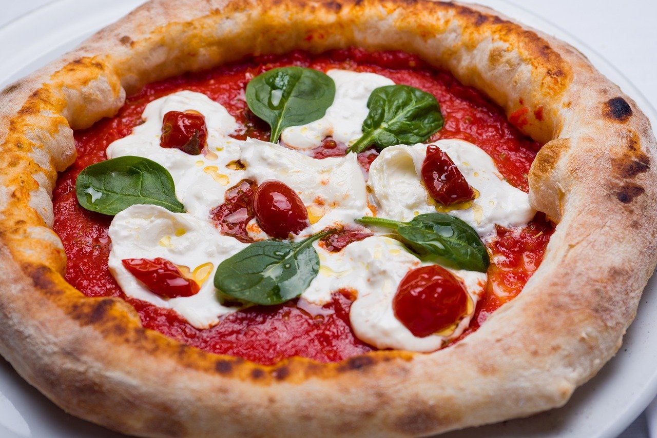 Närbild av en utsökt napolitansk pizza med färsk tomatsås, mozzarellaost, spenatblad och körsbärstomater