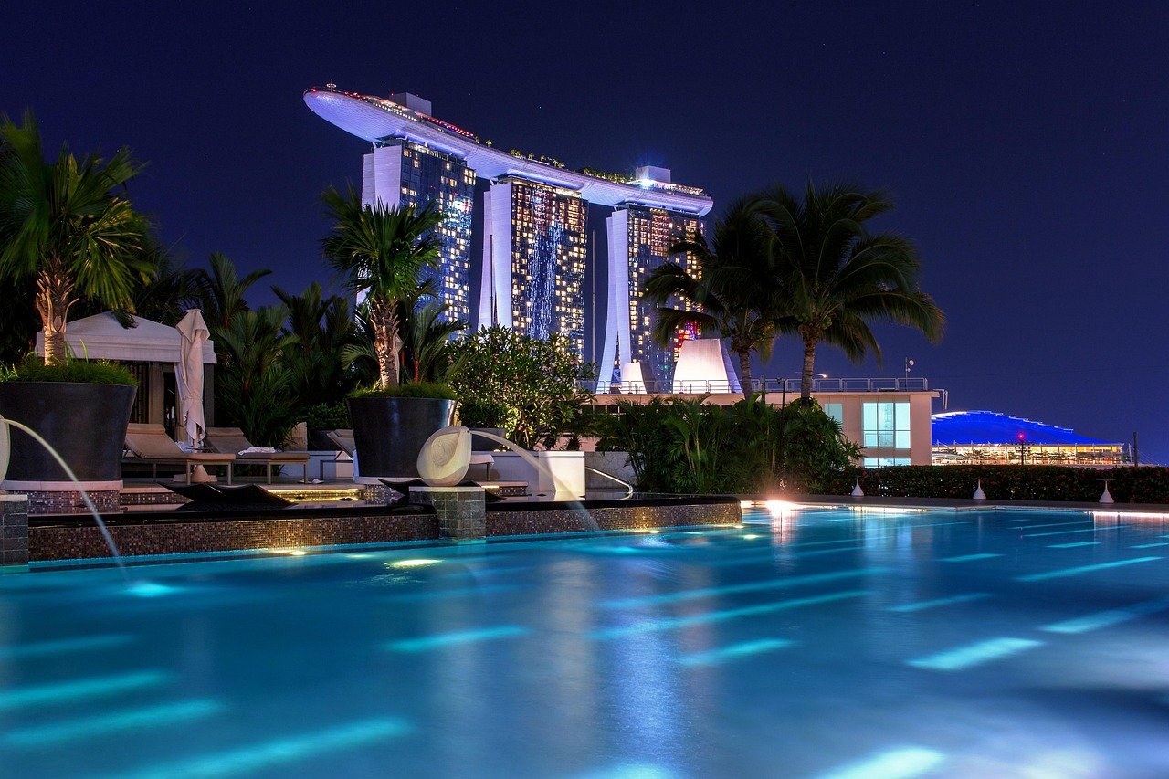 Nattvy av Marina Bay Sands hotell och upplyst takpool i Singapore med palmer och blått vatten