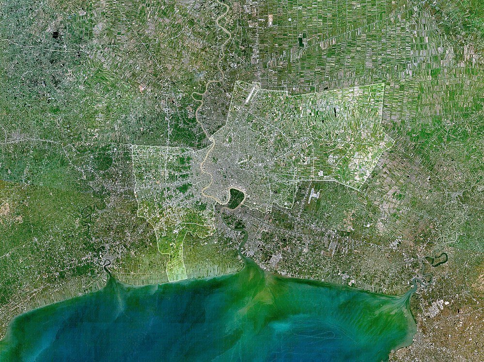 Kuststad satellitvy med floder och jordbruksmark Satellitbild som visar en kuststad med floder, urbana områden och jordbruksfält nära en stor vattenmassa.