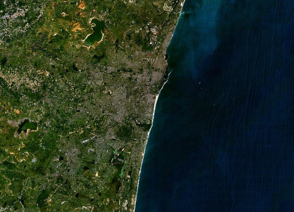 Satellitbild av kuststad och hav Satellitvy av en kuststad med urbana områden, gröna landskap och havskust, som visar detaljerade land- och vattenfunktioner.