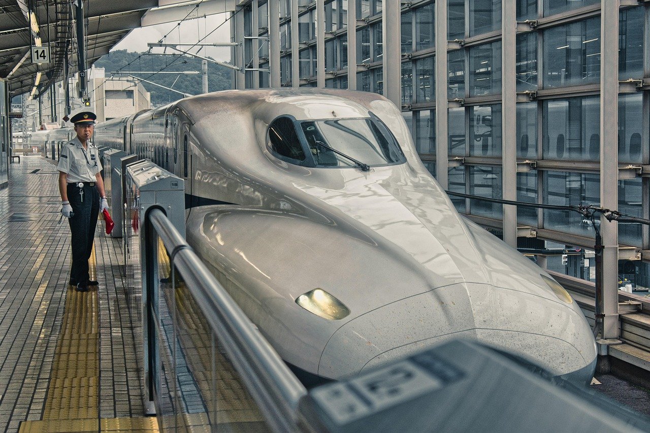 Modern japansk Shinkansen snabbtåg på plattform med uniformerad järnvägspersonal i livlig station