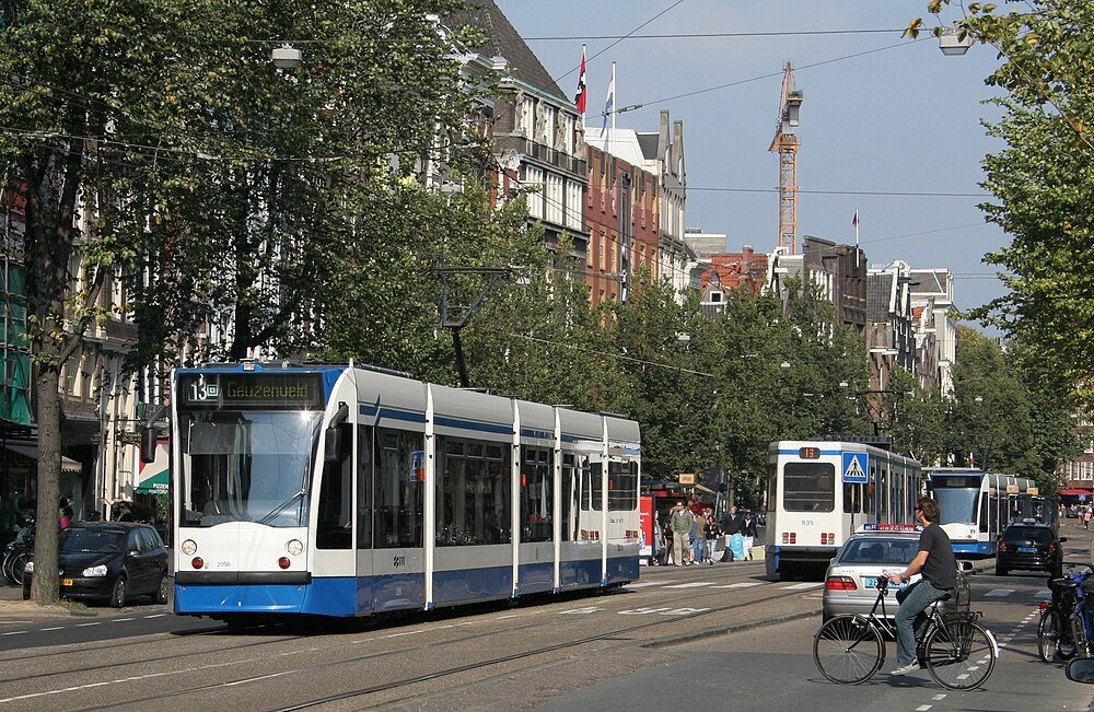 Blå och vit spårvagn på livlig Amsterdams gata Modern blå och vit spårvagn som rör sig genom en livlig stadsgata med cyklister och bilar i Amsterdams stadskärna