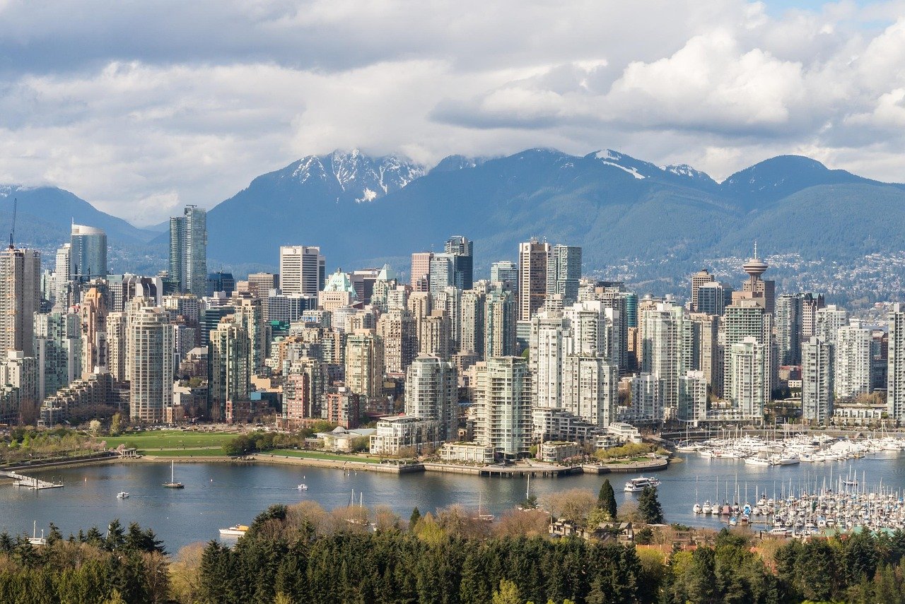 Vancouvers stadsbild med moderna höghus, vattnet och bergen i bakgrunden under molnig himmel