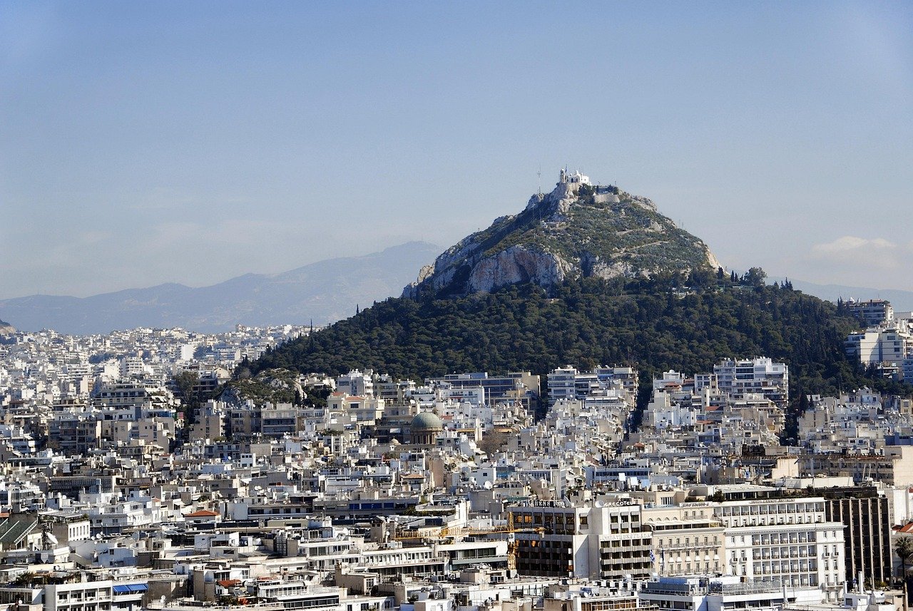 Panoramautsikt över Atens stadsbild med berget Lycabettus täckt av grönska och byggnader under klarblå himmel