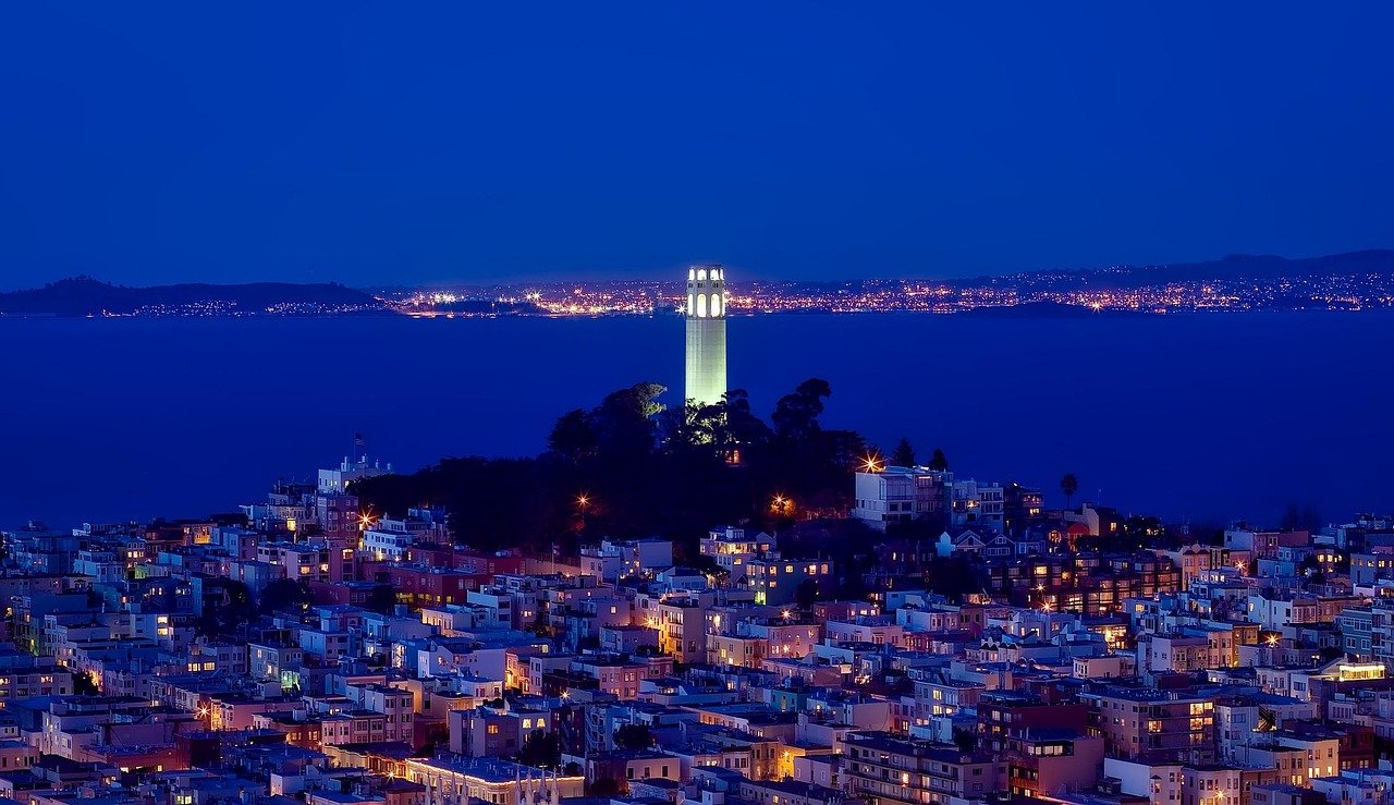 Nattvy av Coit Tower upplyst på Telegraph Hill med utsikt över San Franciscos stadsbild och bukt med avlägsna ljus