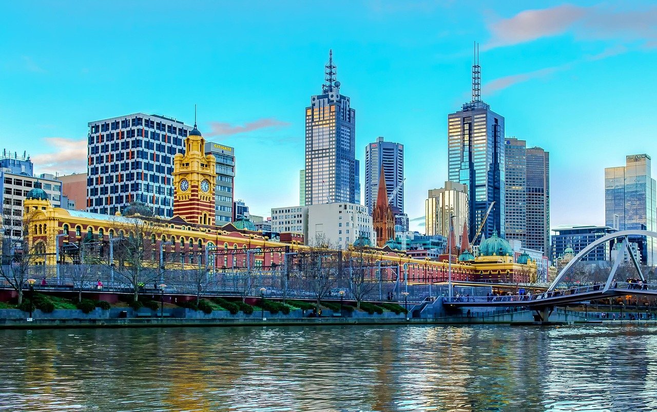 Melbournes stadssilhuett med Yarra River, Flinders Street Station och moderna skyskrapor under en klarblå himmel