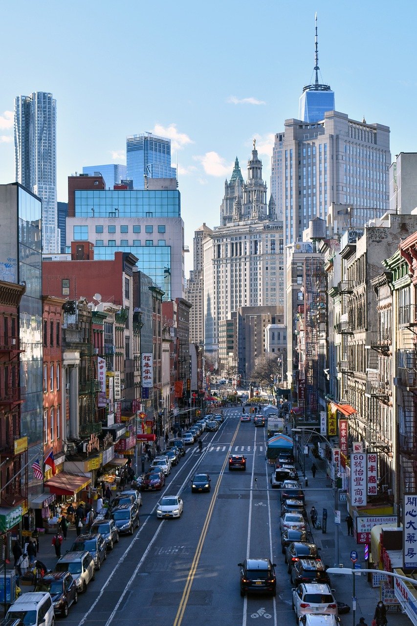 Livlig urban gata i Chinatown med parkerade bilar, fotgängare och höga skyskrapor i bakgrunden under en klar himmel