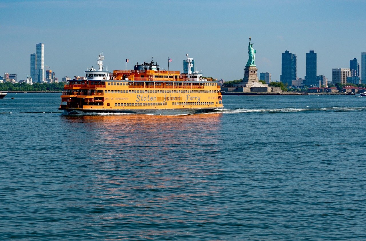 Staten Island Ferry som kryssar i New York Harbor med Frihetsgudinnan och stadssilhuett i bakgrunden på en klar dag