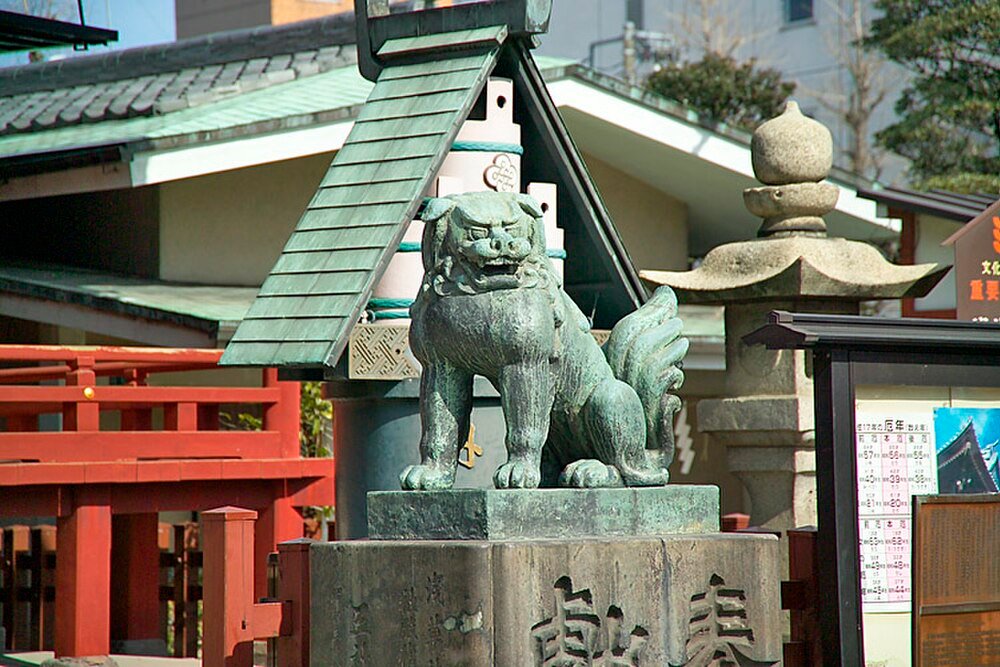 Bronsskulptur av Komainu vid japansk helgedom Bronsskulptur av komainu lejonhund vid en traditionell japansk helgedom med röda trästaket och stenlyktor