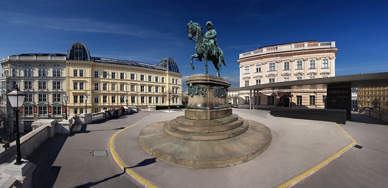 Ryttarstaty framför historiska byggnader och Albertina Museum i Wien under klarblå himmel