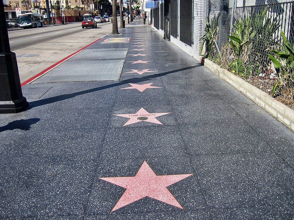 Hollywood Walk of Fame-stjärnor på trottoaren Hollywood Walk of Fame-stjärnor inbäddade i trottoaren längs en livlig gata med bilar och byggnader i bakgrunden