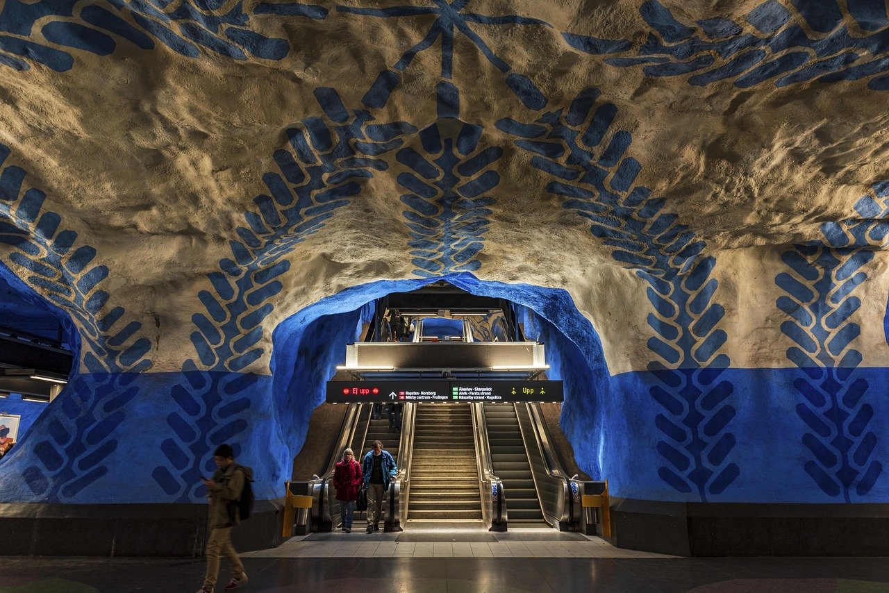 Färgglad underjordisk tunnelbanestation med konstnärliga blå och beige grottliknande väggar och rulltrappor i Stockholm, Sverige