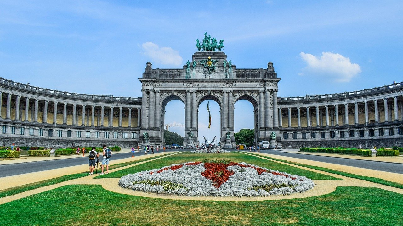 Triumfbågsmonument med statyer och blomsterträdgård i Brysselpark under blå himmel