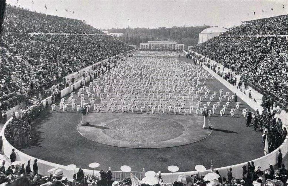 Historisk stadion med synkroniserade idrottare och publik Historisk svartvit foto av en stor stadion fylld med åskådare och idrottare som utför synkroniserade övningar på fältet