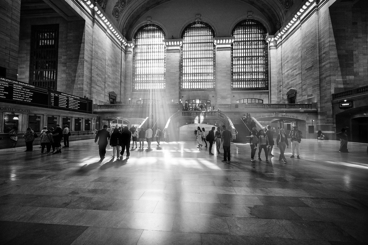 Svartvitt bild av Grand Central Terminal med solljus som strömmar genom stora fönster och människor som går inuti
