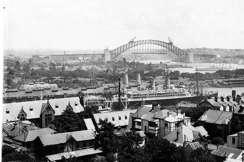 Sydney Harbour Bridge under konstruktion med fartyg Historisk svartvit foto av Sydney Harbour med ett stort fartyg förtöjt och Sydney Harbour Bridge under konstruktion