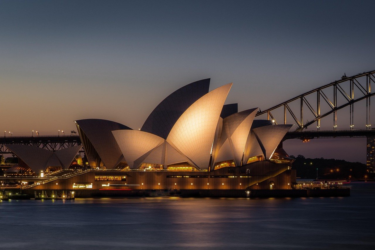 Sydney Opera House upplyst i skymningen med Sydney Harbour Bridge i bakgrunden, ikoniskt australiensiskt landmärke