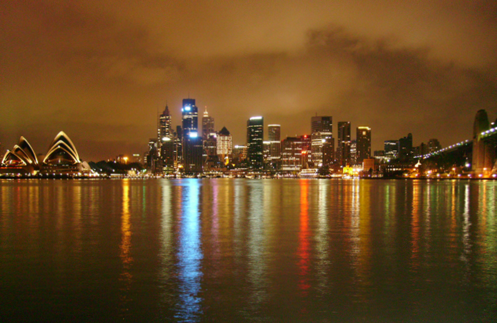 Sydney skyline på natten med Operahus och Harbour Bridge Nattvy av Sydney skyline med upplyst Operahus och Harbour Bridge som reflekteras i vattnet