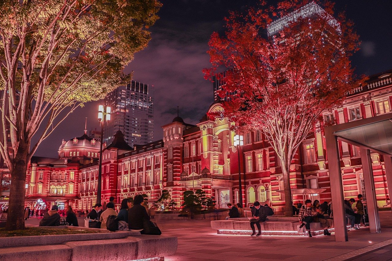 Nattvy av Tokyo Station med upplyst röd tegelbyggnad och människor som sitter under höstträd