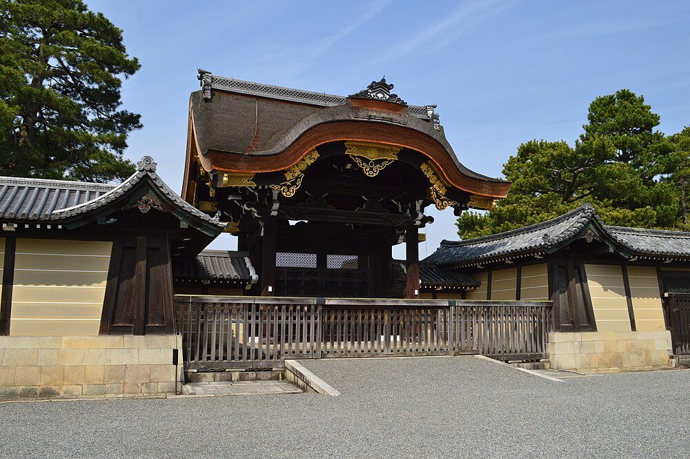 Traditionell japansk tempelport med utsmyckat trätak och omgivande väggar under klarblå himmel