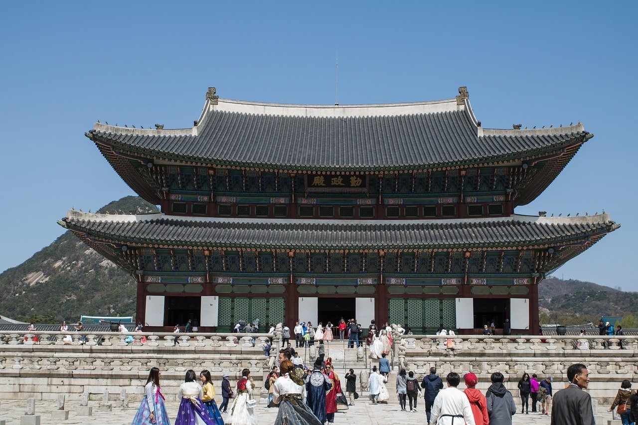 Traditionellt koreanskt palats med turister som bär hanbok-klänningar under klarblå himmel