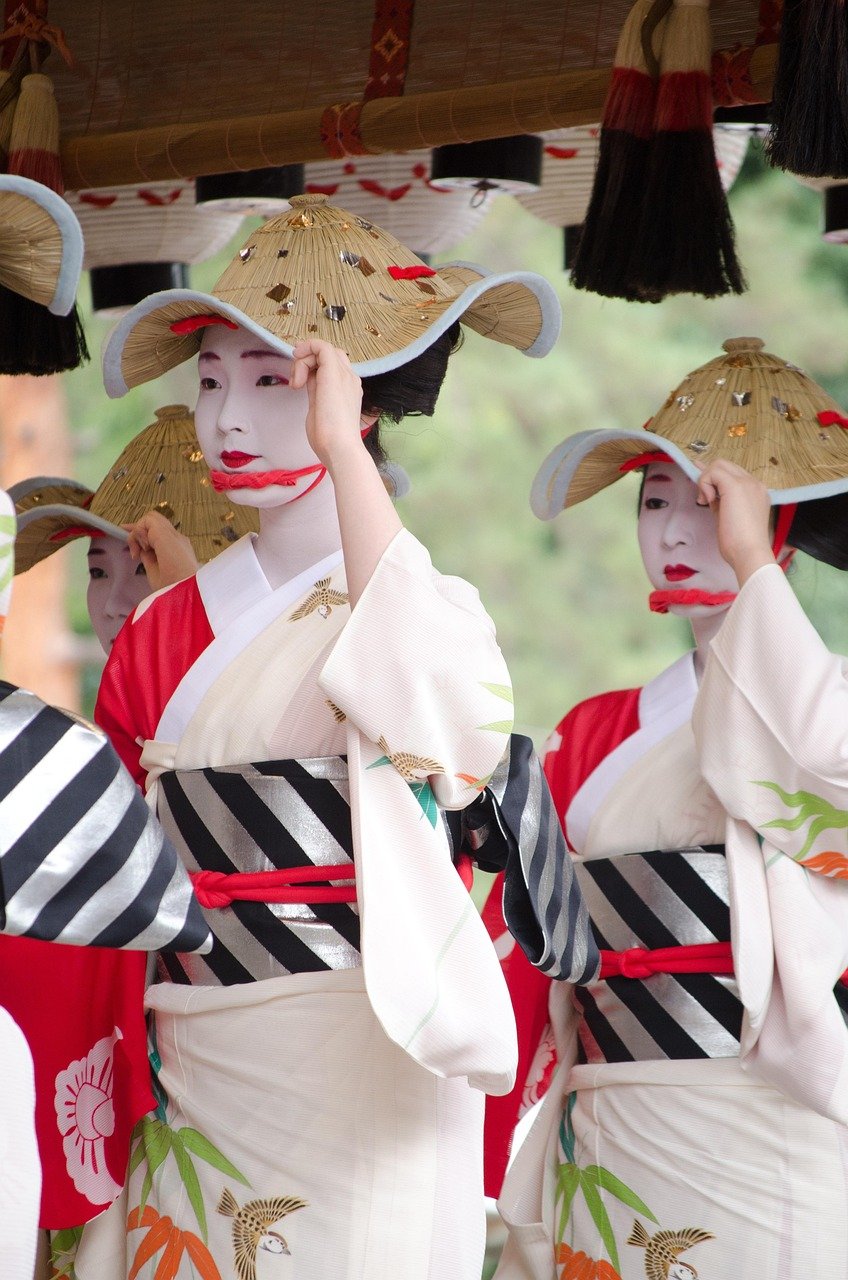 Traditionella japanska kvinnor i vita kimonos och stråhattar som utför en kulturell dans med målade ansikten