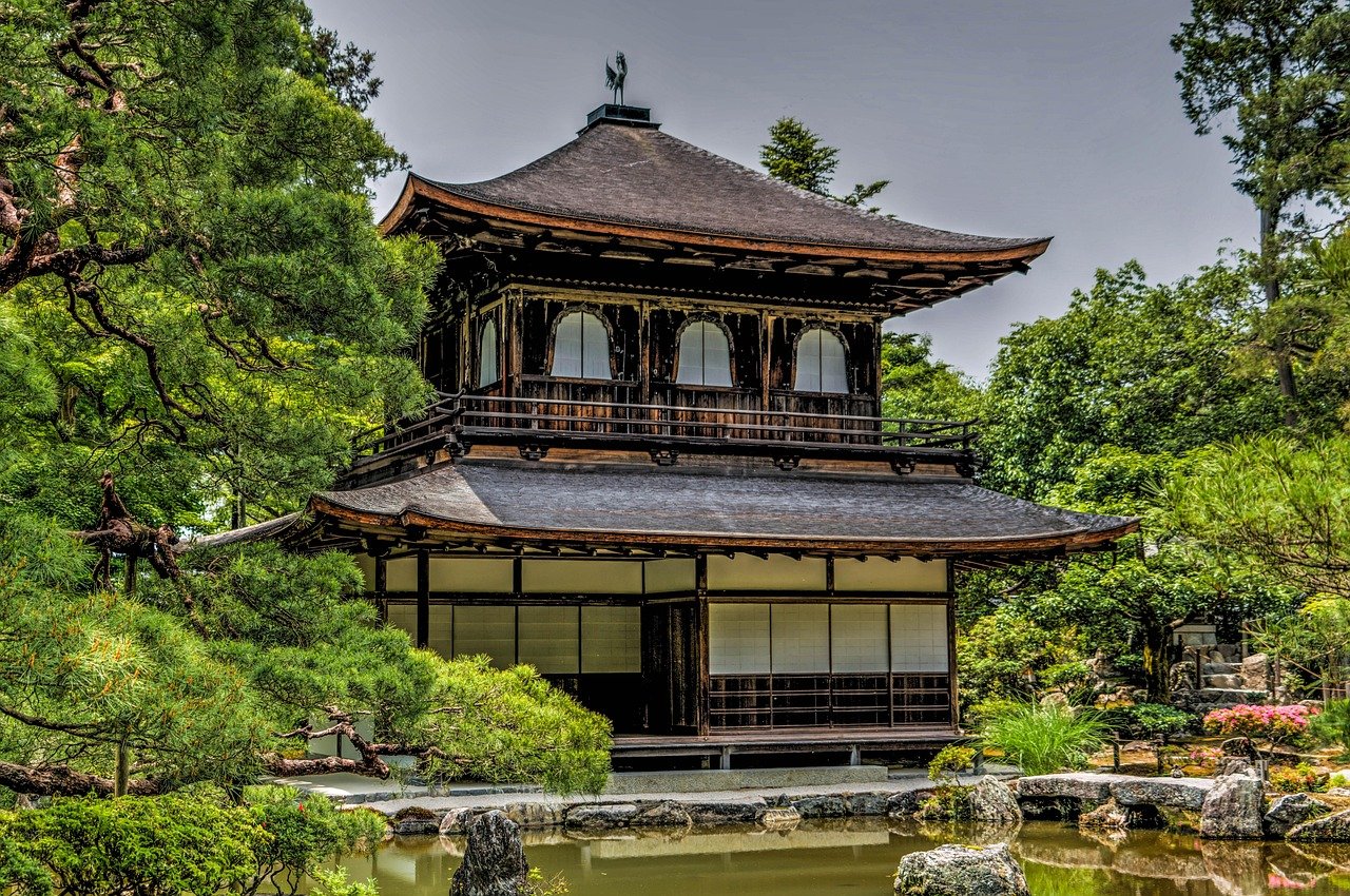 Traditionellt japanskt trätempel omgivet av frodiga gröna träd och en fridfull damm i en lugn trädgårdsmiljö