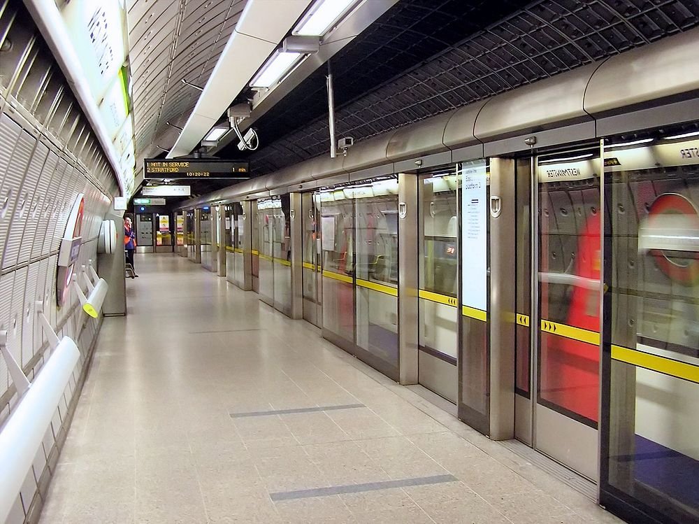 Londons tunnelbaneplattform med tågankomstdisplay Tom plattform i Londons tunnelbana med säkerhetsglasdörrar och digital tågankomstdisplay