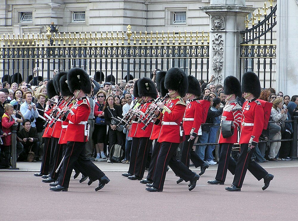 Brittiska vakter marscherar vid Buckingham Palace Brittiska vakter i röda uniformer och björnskinnshattar marscherar och spelar instrument vid Buckingham Palace-ceremoni