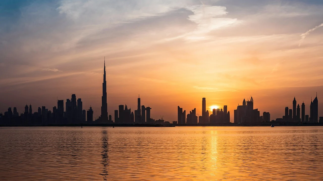 Dubais skyline vid solnedgången med Burj Khalifa Solnedgångsvy över Dubais skyline med Burj Khalifa och moderna skyskrapor som speglas i lugnt vatten