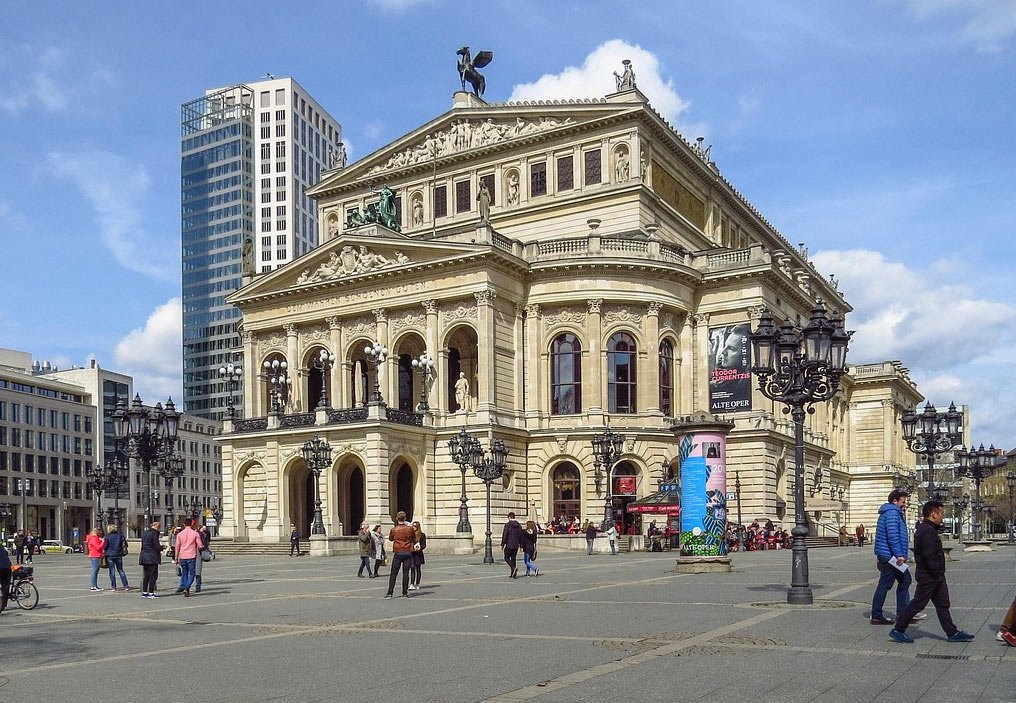 Historiska Alte Oper-byggnaden i Frankfurt med människor som promenerar och moderna skyskrapor i bakgrunden på en solig dag