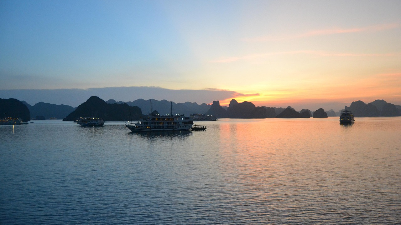 Solnedgång och båtar i Ha Long Bay, Vietnam Solnedgång över lugnt hav med traditionella båtar och kalkstensöar i Ha Long Bay, Vietnam, som visar upp lugn naturlig skönhet.