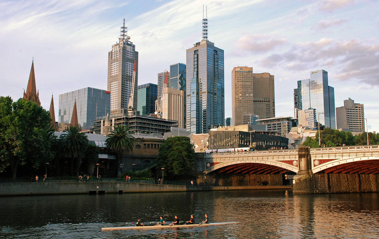 Melbournes silhuett med Yarra River och roddare Melbournes stadssilhuett med Yarra River, moderna skyskrapor, historiska byggnader och ett roddlag på vattnet vid solnedgången