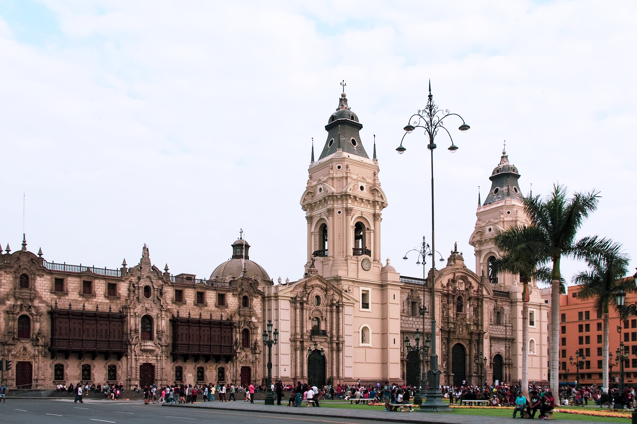 Lima Plaza Mayor Katedral och Regeringspalats Historisk kolonial katedral och regeringspalats på Limas Plaza Mayor med turister och palmer under molnig himmel
