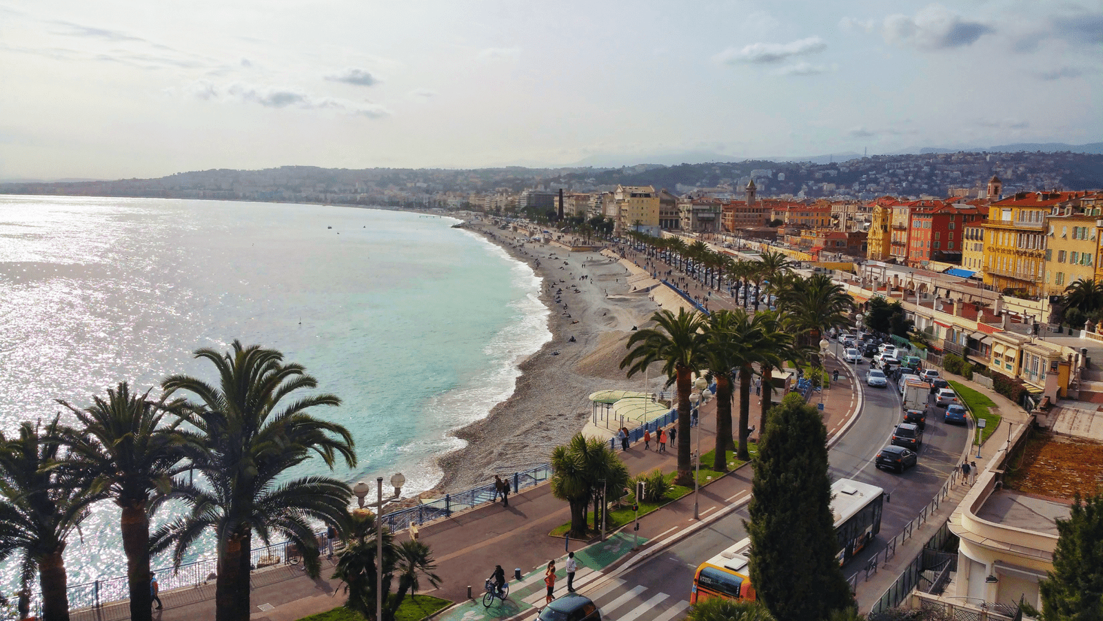 Nice Promenade des Anglais Strand- och Stadsutsikt Scenisk vy över Nice Promenade des Anglais med palmer, stenstrand, turkost hav och livlig stadsbild i Frankrike