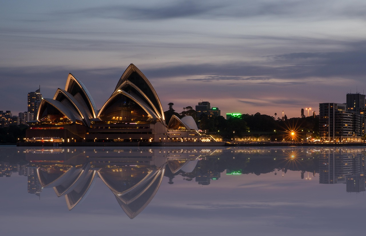 Sydney Opera House i skymningen med stadssilhuett Sydney Opera House upplyst i skymningen med stadssilhuett och vattenreflektion i Sydney, Australien