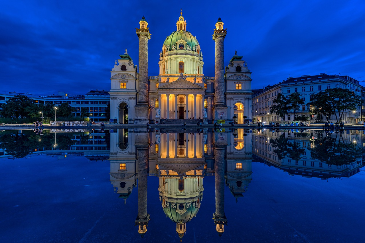 Historisk upplyst kyrka vid skymningen med reflektion Upplyst historisk kyrka med tvillingkolonner reflekterade i vattnet vid skymningen i en europeisk stad