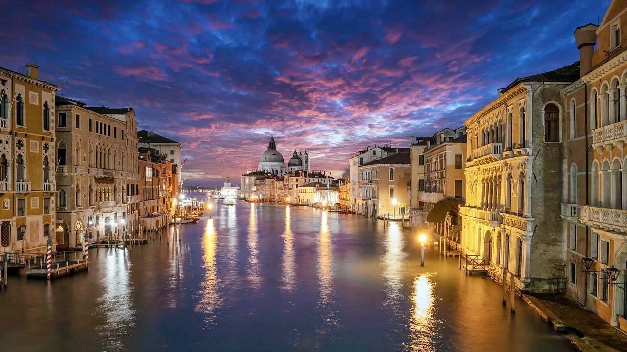 Venedigs kanal solnedgång med historiska byggnader Venedigs kanal vid solnedgången med historiska byggnader och en livfull himmel som speglas i vattnet, ikonisk italiensk stadsbild
