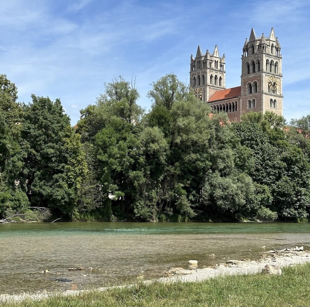 De två tornen på St. Maximilian-kyrkan ovanför Isars gröna stränder i München
