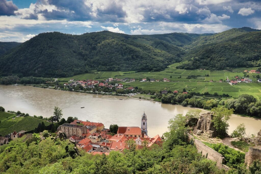 Flygbild över Dürnstein vid Donau i Wachau-dalen, med vingårdar och ett blått barockt kyrktorn, en dagsutflykt från Wien